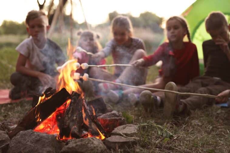 Kinder einer Jugendfreizeit rösten Marschmallows über einem Lagerfeuer